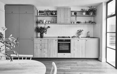 black and white photograph of a kitchen with wooden cabinets, an oven, potted plants, and a dining room table