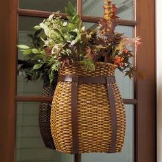 a basket hanging from the side of a door with flowers in it and leaves on top