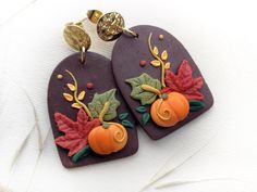 two purple heart shaped earrings decorated with autumn leaves and pumpkins on top of each other