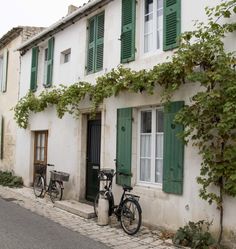 two bikes are parked in front of an old building with green shutters and windows