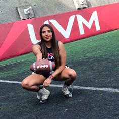 a beautiful young woman holding a football on top of a field