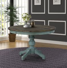 a round wooden table sitting on top of a rug in front of a gray wall