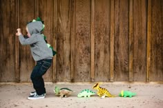 a little boy playing with toy dinosaurs in front of a wooden wall and wood fence