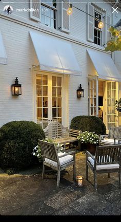 two chairs and a table in front of a white building with flowers on the ground