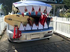 a surfboard is strapped to the back of a car in front of a white picket fence