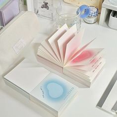 an open book sitting on top of a white desk next to a cup and pen