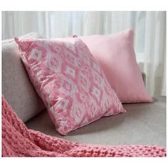 pink and white pillows sitting on top of a gray couch