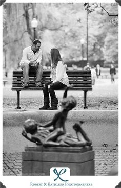 a man and woman sitting on a park bench next to a statue in black and white