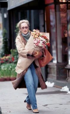 a woman is walking down the street with flowers in her hand and she is carrying a bag