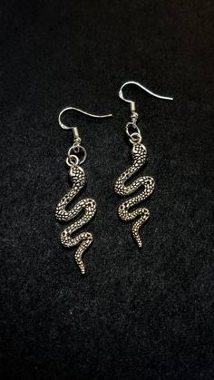 This listing is for 1 pair of new, made to order, Tibetan Silver Snake Earrings. They are on Hypoallergenic Fish Hook Style posts. Please view all photos for size reference.  Snake Symbolism: Fertility and rebirth Historically, serpents and snakes represent fertility or a creative life force. As snakes shed their skin through sloughing, they are symbols of rebirth, transformation, immortality, and healing. The ouroboros is a symbol of eternity and continual renewal of life. Professionally packag Handmade Snake Shape Earrings, Snake Symbolism, Snake-shaped Earrings For Gifts, Silver Snake-shaped Pierced Earrings, Silver Snake-shaped Single Earring, The Ouroboros, Silver Snake-shaped Metal Earrings, Snake Shedding, Earrings Snake