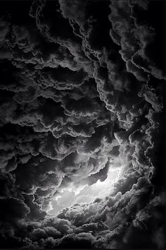 black and white photograph of clouds in the sky with sun peeking through it's center