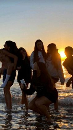 a group of people standing in the ocean at sunset