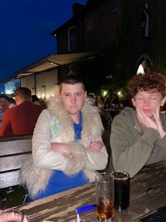 two people sitting at a table with drinks in front of them and one person holding his hand to his face