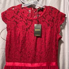 a red dress hanging on a hanger in front of a white shirt with a tag