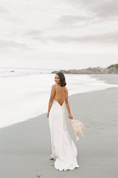 a woman in a white dress is walking on the beach with her back to the camera