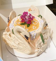 a decorated cake in a box with flowers on the top and two swans on the bottom