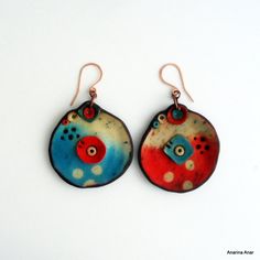 pair of earrings with red, blue and white designs on them hanging from copper ear wires