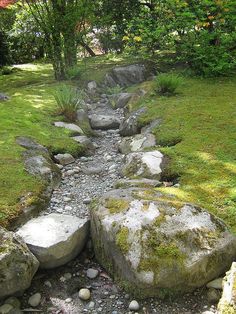 a stream running between two large rocks in the middle of a grassy area with trees