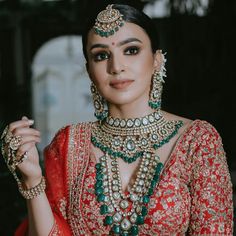 a woman in a red and gold bridal outfit with green jewelry on her neck