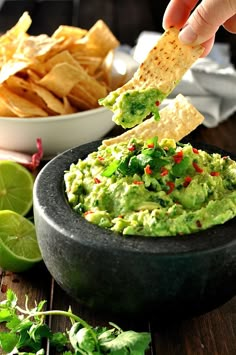 a person dipping guacamole into a bowl with tortilla chips on the side