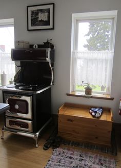 an old fashioned stove in the corner of a room with two windows and a rug on the floor