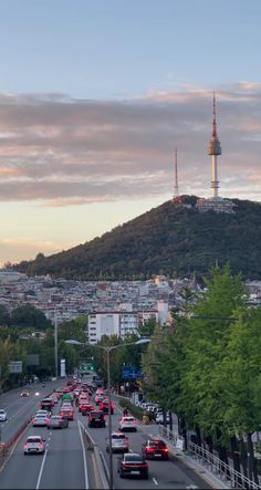 cars are driving down the road in front of a hill with a television tower on top