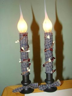 two candles are decorated with plaid fabric and bows on the top one is turned upside down