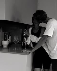 a man and woman standing next to each other in front of a counter with wine glasses