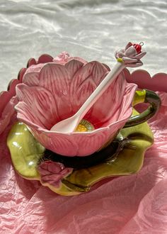 a pink flower sitting on top of a green bowl with a spoon in it's center