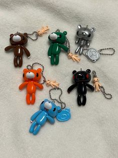 six different colored teddy bears are on a white sheet and one is holding a keychain