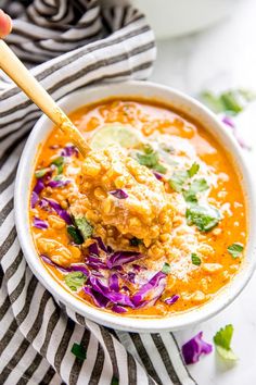 a hand holding a wooden spoon over a bowl of mexican chicken tortilla soup