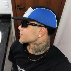 a man with a tattoo on his neck wearing sunglasses and a hat sitting in front of a sink