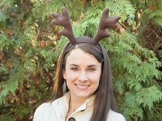 a woman with deer antlers on her head smiles at the camera while standing in front of some trees