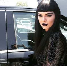 a woman with black lipstick standing next to a car