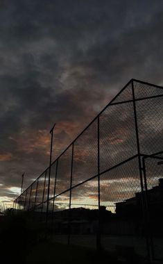 the sky is dark and cloudy behind a fence