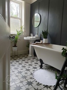 a white bath tub sitting next to a sink in a bathroom under a window with potted plants