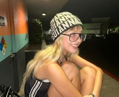 a blonde woman wearing glasses and a knitted hat sitting next to a parked bike