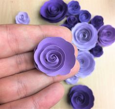 a hand holding a small purple flower on top of a wooden table next to smaller purple flowers