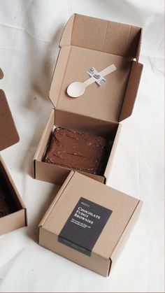 two boxes with brownies in them on a white tablecloth and one has a spoon