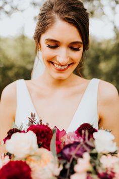 a woman holding a bouquet of flowers in her hands and smiling at the camera while wearing a white dress