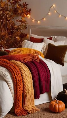 a white bed topped with pillows and blankets next to a tree filled with fall leaves