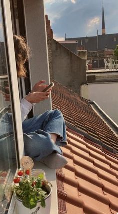 a woman sitting on top of a window sill looking at her cell phone