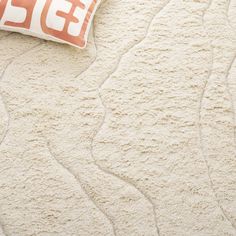 an orange and white pillow sitting on top of a bed next to a beige rug