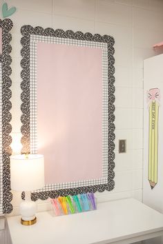 a white desk with a pink mirror and pencils on the table next to it