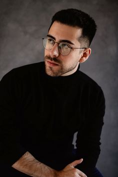 a man wearing glasses sitting down with his arms crossed