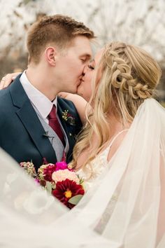 a bride and groom kissing each other in front of a veiled backdrop with flowers