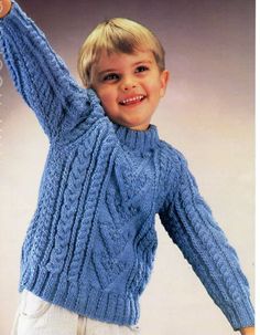 a young boy wearing a blue cabled sweater and holding his arm up in the air