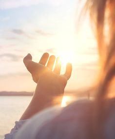 a person holding their hand up to the sun in front of some water and clouds