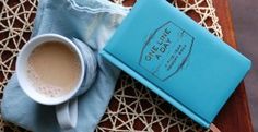 a cup of coffee next to a blue book on a doily with a lace edge