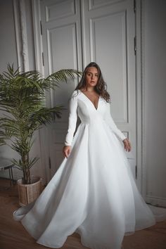 a woman in a white wedding dress standing next to a potted plant